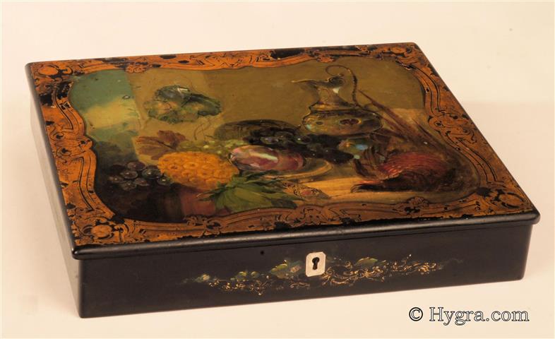 Papier mch writing box the top painted with a still life of fruit and game, framed  by gilded decoration. Inlays of mother of pearl are used to give a translucence to the painting. Th box is embossed to the base "JENNENS & BETTRIDGE".  The box opens to a sloping velvet covered writing surface and a lift out tray still covered in its original paper. The box has two original inkwells and a working lock and key. Circa 1830. -Enlarge Picture